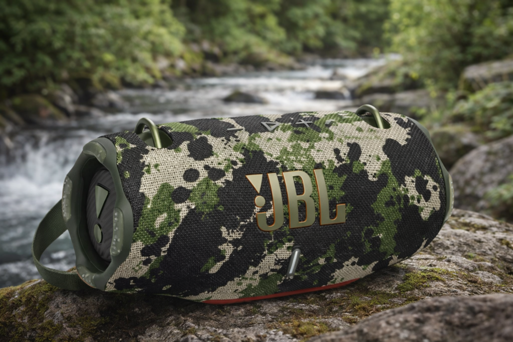 JBL Xtreme 4 with camouflage fabric exterior placed on rock beside flowing water with forest background